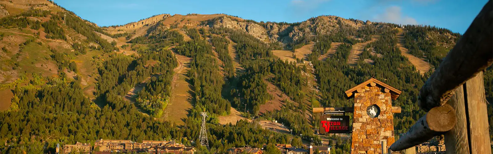 Ski slopes in the off season behind the welcome sign to Teton Village, WY.